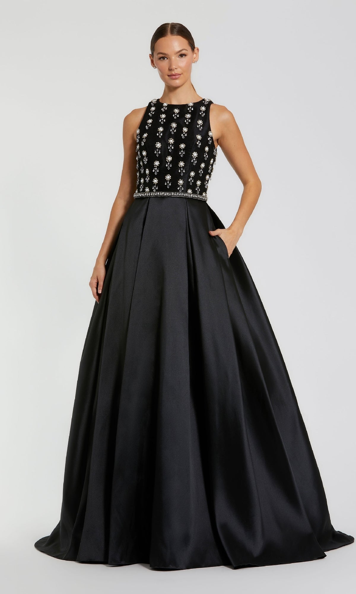 A woman wearing the Mac Duggal 48803 long formal dress, featuring a sleeveless black design with a jewel-embellished bodice and satin A-line skirt, poses against a plain background.